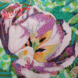 Può includere: Primo piano di un fiore rosa e bianco realizzato con ritagli di tessuto. Il fiore è circondato da un tessuto a fantasia verde e blu.