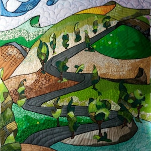 Può includere: Un paesaggio trapuntato con una strada grigia tortuosa attraverso colline e alberi verdi. La trapunta utilizza varie tonalità di tessuto verde, marrone e blu. Un disegno blu a forma di onda nella parte superiore suggerisce un cielo o l'acqua.