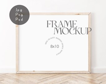 May include: A white frame mockup with a light wood frame, sitting on a light wood floor with a white wall in the background. The frame is 8x10 inches and has the text "FRAME MOCKUP" in gray text.