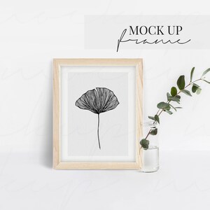 K&ouml;nnte beinhalten: Ein gerahmter schwarz-wei&szlig;er Kunstdruck mit einer detaillierten Strichzeichnung einer Blume. Das Kunstwerk befindet sich in einem hellen Holzrahmen. &Uuml;ber dem Rahmen steht der Text "MOCK UP frame". Neben dem Rahmen steht eine kleine Glasvase mit Gr&uuml;nzeug.