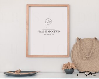 May include: A wooden frame mockup with the text "FRAME MOCKUP" and "files Psd Png Jpg" printed on a white background. The frame is on a white shelf with a woven bag, a small bowl of dried flowers, and a pair of glasses.