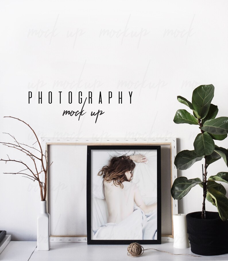 May include: A black framed photo mockup with a white background and a woman lying on a white bed. The photo is on a white shelf with a white vase and a small plant. The text "PHOTOGRAPHY mock up" is written on the wall behind the photo.