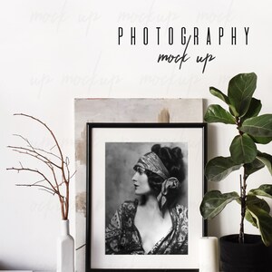 May include: Black and white photo of a woman wearing a headscarf, framed in a black frame, on a white shelf with a vase of branches, a candle, and a ball of twine. The text "PHOTOGRAPHY mock up" is written on a white wall behind the shelf.