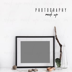 May include: A black framed photo mockup with a gray background, a book, a wooden bowl, and a twig in a glass vase on a white surface. The text "PHOTOGRAPHY mock up" is written above the frame.