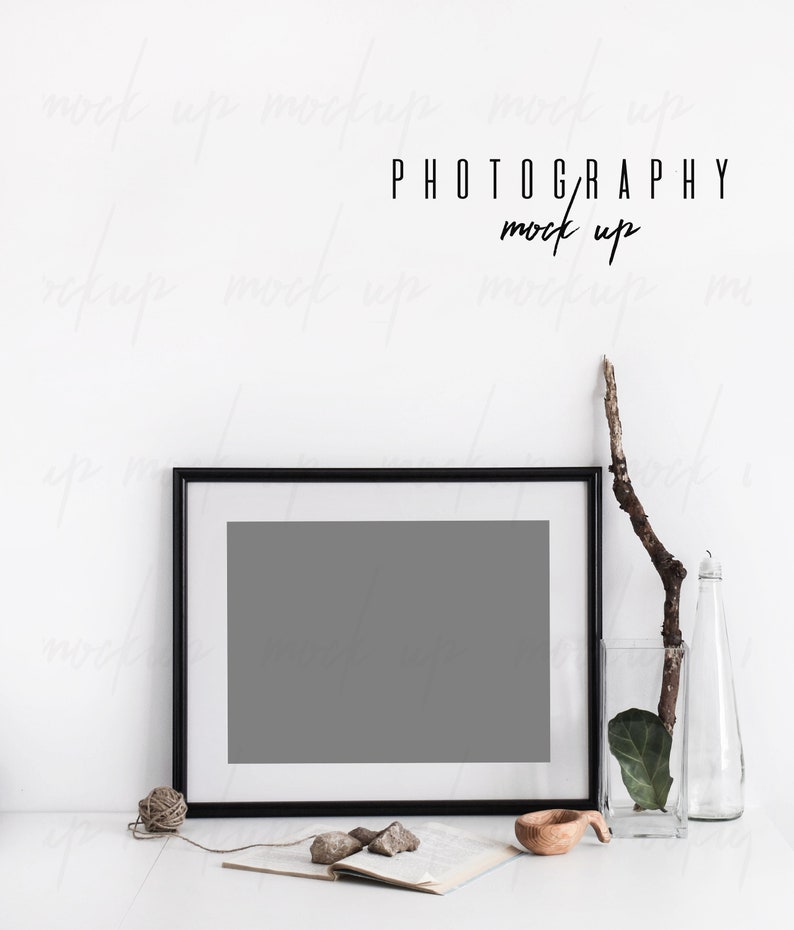 May include: A black framed photo mockup with a gray background, a book, a wooden bowl, and a twig in a glass vase on a white surface. The text "PHOTOGRAPHY mock up" is written above the frame.
