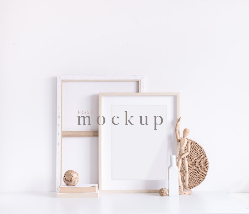 May include: Two wooden picture frames with white mounts, one slightly larger than the other, are leaning against a white wall. The frames are empty and ready for a photo or artwork. A small wooden figurine and a wicker basket are on a white surface in front of the frames.
