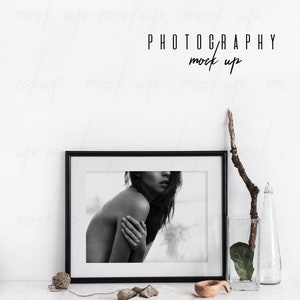 May include: Black and white photo of a woman in a black frame on a white surface with a wooden bowl, a book, and a vase with a branch and a leaf. The text "PHOTOGRAPHY mock up" is above the frame.
