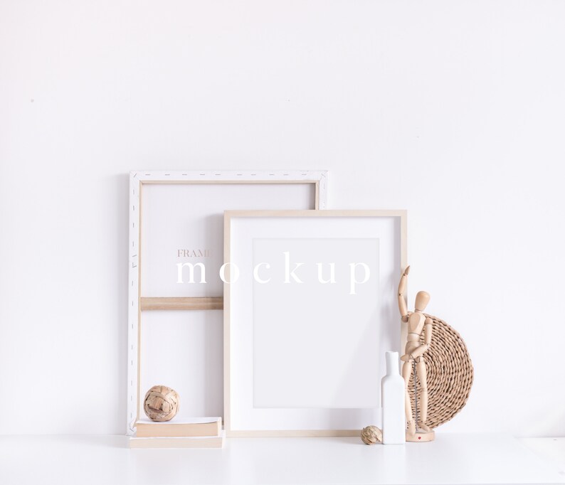 May include: Two wooden picture frames with white mounts, one larger than the other, are leaning against a white wall. The frames are empty and ready for a photo or artwork. A wooden figurine, a small ball, and a white vase are on a white surface in front of the frames.