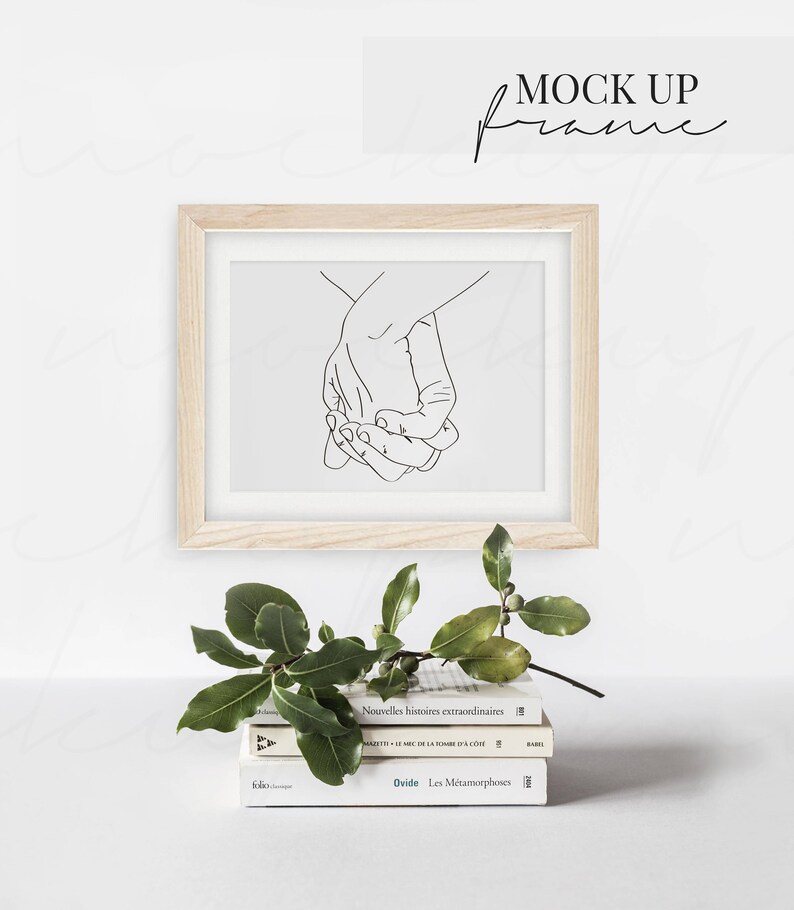 May include: A wooden frame with a white mat and a black line drawing of two hands holding each other. The frame is sitting on a stack of three books with the titles "Nouvelles histoires extraordinaires", "MAZETIC DE LA TOME DA COM", and "Ovide. Les M&eacute;tamorphoses".