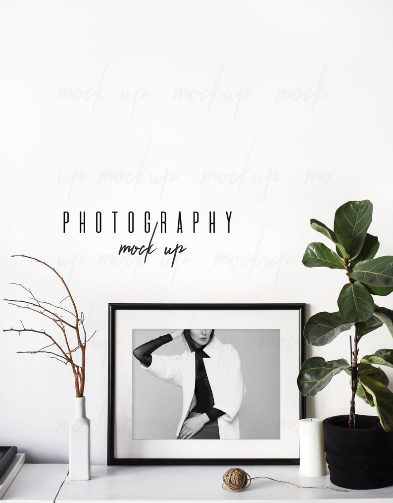 May include: Black and white photo of a person wearing a white jacket and black shirt in a black frame on a white shelf with a white vase and a potted plant. The text "PHOTOGRAPHY mock up" is written in black on the white wall behind the frame.