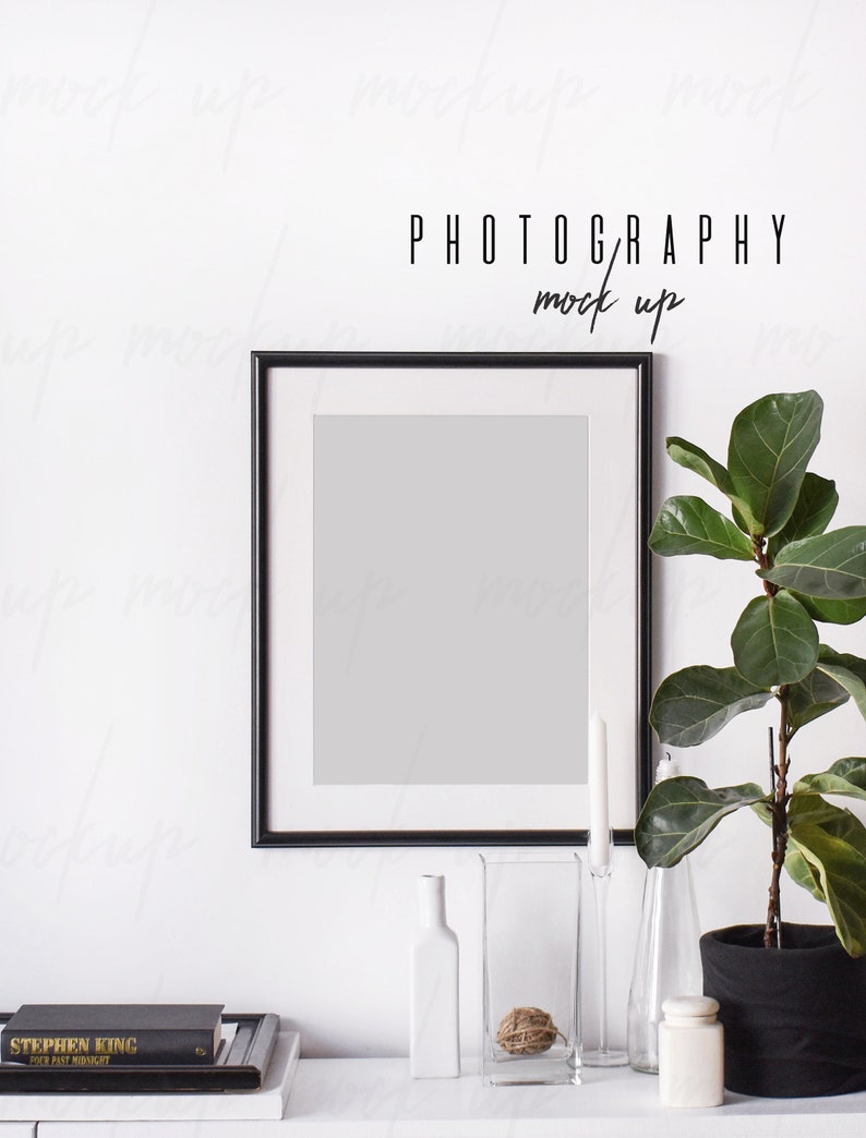 May include: Black framed photo mockup with a white mount, a potted plant, and decorative glass vases on a white surface. The text "PHOTOGRAPHY mock up" is above the frame.