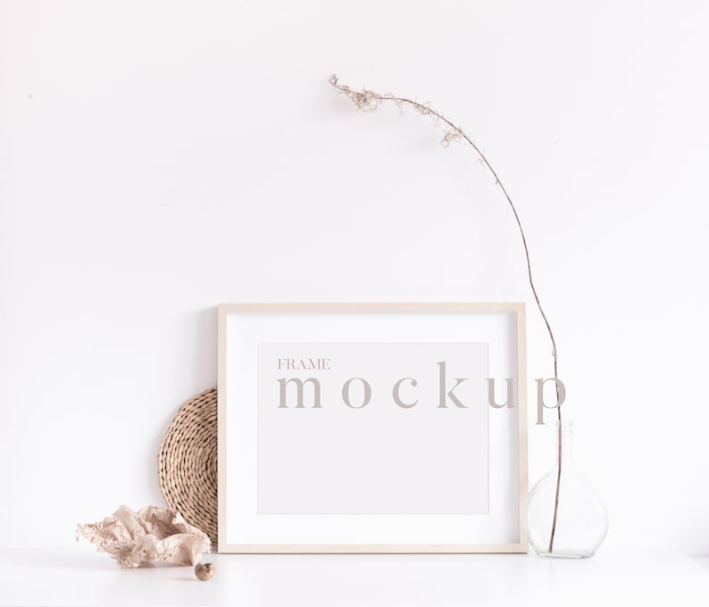 Peut inclure: Une maquette de cadre blanc avec le texte "FRAME MOCKUP" sur un fond blanc. Une branche s&eacute;ch&eacute;e dans un vase en verre transparent et un dessous de verre en osier sont sur une surface blanche.
