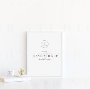 May include: White frame mockup with the text "FRAME MOCKUP" and "files Psd Png Jpg" on a white surface with a small cactus and candle.