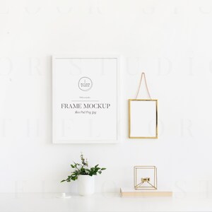 May include: White frame mockup with a gold frame hanging above a white table with a small potted plant and a gold candle holder. The text on the white frame reads "FRAME MOCKUP 11x14 inches".