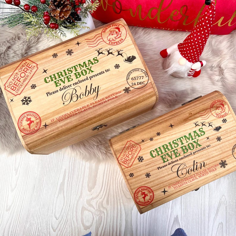 May include: Two rectangular wooden boxes with hinged lids, each printed with Christmas Eve Box, North Pole Express stamps, reindeer silhouettes, and snowflakes. One box is personalized with the name Bobby and the other with the name Colin.