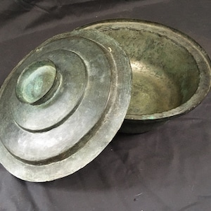 May include: A vintage, green metal pot with a lid. The pot has a rounded shape and a smooth surface. The lid has a raised centre and a decorative rim.