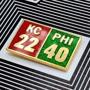 May include: A gold-colored enamel pin with a red and green scoreboard design. The scoreboard shows "KC 22" on the red side and "PHI 40" on the green side. The pin is on a black and white background with the text "Papa Jawns Super Bowl LIX Score - Hard F".
