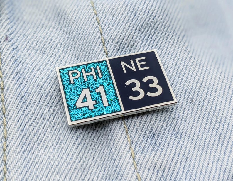 May include: A blue and black enamel pin with the words "PHI 41" and "NE 33" on it.
