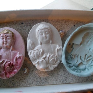 May include: Three decorative plaster wall plaques featuring a Buddha figure with lotus flowers. The plaques are in shades of pink, white, and blue.