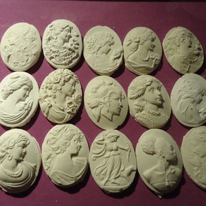 May include: A collection of 15 white oval cameo pendants featuring various designs of women's faces. The pendants are made of a smooth, white material and have a slightly raised design.