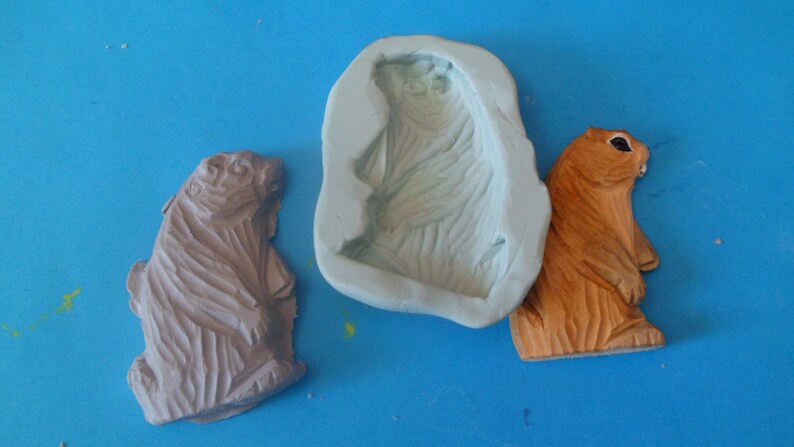 May include: Two brown and orange figurines of a standing groundhog, one is a finished product and the other is a silicone mold.