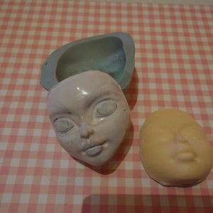 Peut inclure: Deux moules en silicone pour la fabrication de têtes de poupée. Un moule est bleu clair et l'autre est jaune clair. Les deux moules ont un visage détaillé avec des yeux, un nez et une bouche.