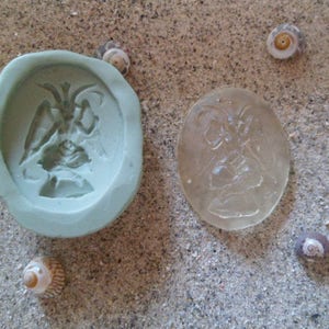 Puede incluir: Un molde de silicona verde y una fundición de resina transparente de un ángel con las alas extendidas.