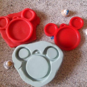 Peut inclure: Trois moules en silicone pour la fabrication d'objets en résine. Un moule est rouge et en forme de tête d'ours avec deux oreilles. Un autre moule est rouge et en forme de tête de Mickey Mouse avec deux oreilles. Le troisième moule est bleu clair et en forme de tête d'ours avec deux oreilles et un nez.