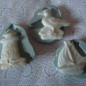 Puede incluir: Tres moldes de silicona para hacer decoraciones de pasteles. Los moldes tienen forma de faro, velero y gaviota. Los moldes son de color azul claro y blanco.
