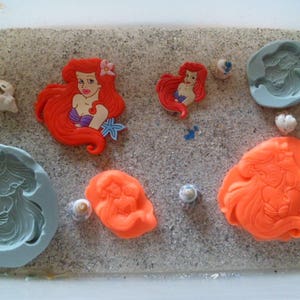 May include: A set of silicone molds for making mermaid-themed cake decorations. The molds are in various shades of blue and orange, and feature different mermaid designs.