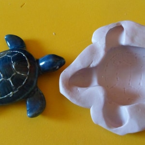 Puede incluir: Una figurita de tortuga de cerámica azul y un molde de silicona morado para hacer una figurita de tortuga.