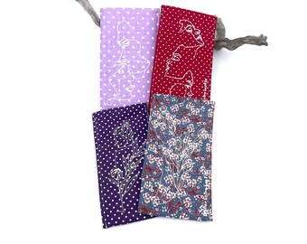 May include: Four fabric pouches with different patterns. The pouches are purple with white polka dots, red with white polka dots, purple with white polka dots and a white floral design, and blue with white polka dots and a white floral design.