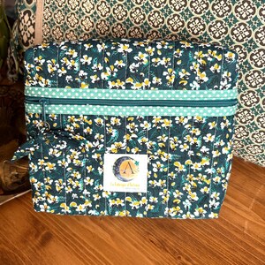 Può includere: Una pochette verde con cerniera, con un motivo floreale bianco e un bordo a pois verde e bianco. La pochette ha una piccola pochette con cerniera abbinata, attaccata ad essa. La pochette ha un'etichetta che dice "La Boutique d'Alice".