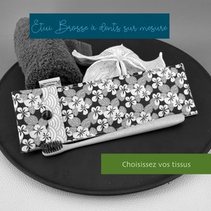 Op de afbeelding: Een zwart-witfoto van een tandenborstel en een bloemenstofhoes. De hoes heeft een knoopsluiting en de tekst "Etui Brosse à dents sur mesure" is zichtbaar. De tekst "Choisissez vos tissus" is ook zichtbaar.