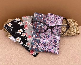 May include: Four patterned fabric eyeglass cases with a pair of black framed glasses on top. The cases are in floral patterns with black, white, pink, blue, and green colours.
