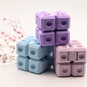 May include: Three fidget cubes stacked on top of each other. The top two cubes are purple and the bottom cube is blue.