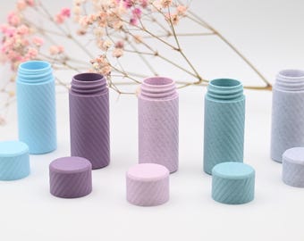 May include: A collection of colorful, textured bottles with matching screw-on lids. The bottles are in shades of blue, purple, and pink. The design features a diagonal, ridged pattern. A sprig of pink flowers is in the background.