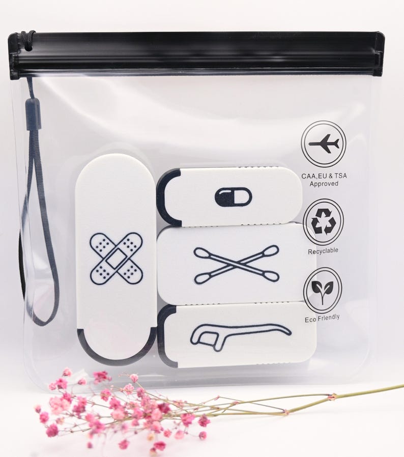 May include: A clear, rectangular plastic travel pouch with a black zipper and wrist strap. Inside are three white rectangular cases with black icons: a bandage, a pill, cotton swabs, and a dental flosser. Text includes CAA, EU & TSA Approved.