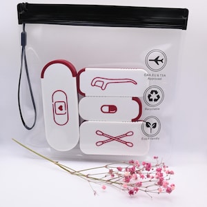May include: A clear plastic travel pouch with a black zipper and wrist strap containing three white rectangular cases with maroon accents. The cases feature icons of a dental flosser, a pill, and cotton swabs. Text includes CAA, EU & TSA Approved.