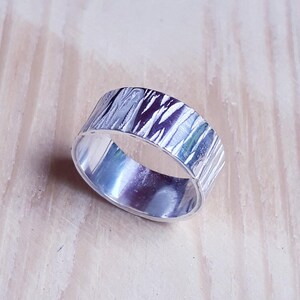 May include: A silver ring with a textured, hammered finish. The ring is wide and has a rounded shape.