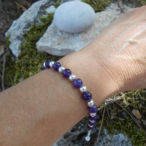 Puede incluir: Un brazalete de cuentas moradas y plateadas con cierre deslizante. El brazalete est&aacute; hecho con peque&ntilde;as cuentas redondas y se lleva en la mu&ntilde;eca.