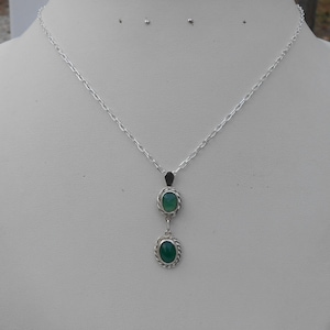 May include: A silver chain necklace with a pendant featuring two oval green gemstones set in silver.