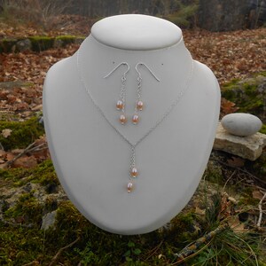 May include: A silver necklace and earrings set with a delicate chain and multiple small pink pearls hanging from the pendant and earrings.