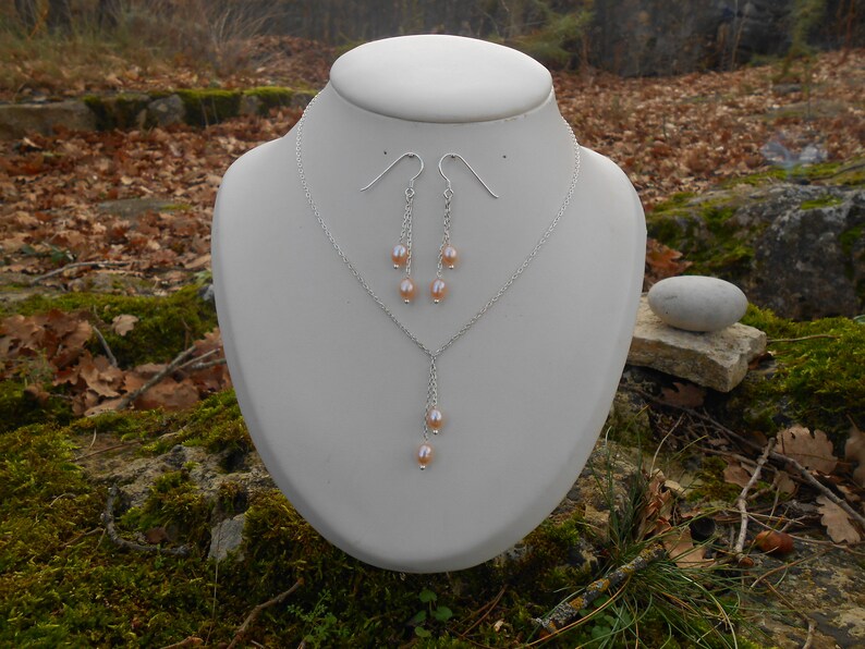 May include: A silver necklace and earrings set with a delicate chain and multiple small pink pearls hanging from the pendant and earrings.