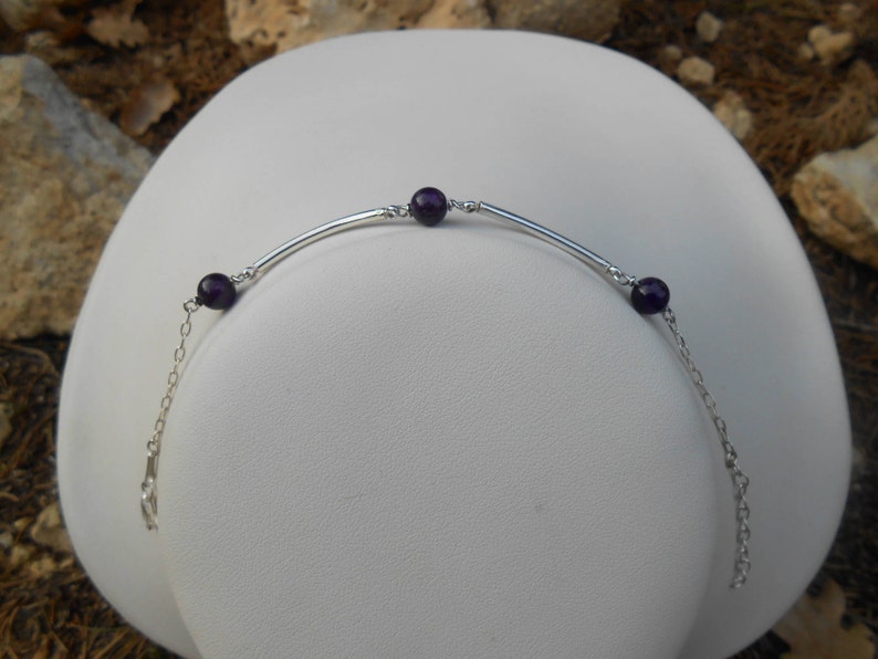 May include: A silver bracelet with a curved bar and three amethyst beads.