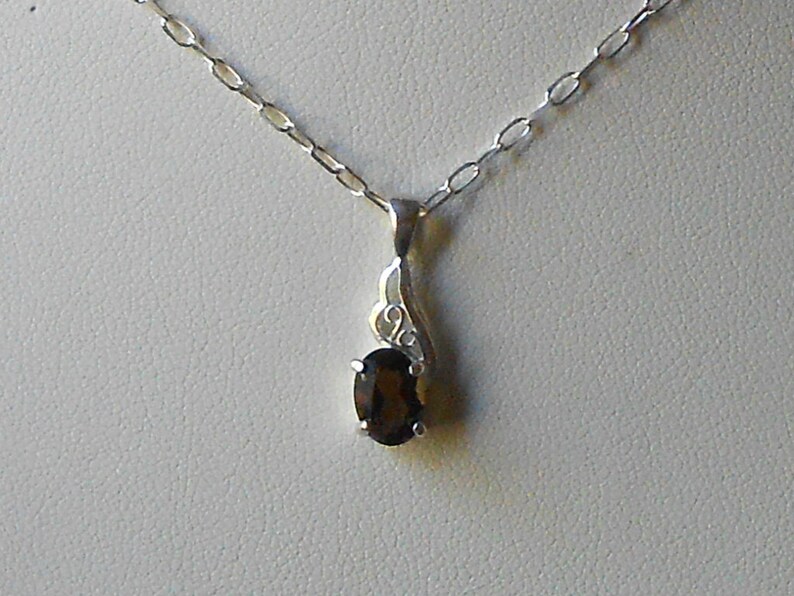 May include: A silver chain necklace with a pendant featuring a dark brown oval gemstone set in a silver swirl design.
