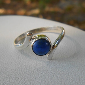 May include: A silver ring with a blue gemstone. The ring has a unique, curved design.