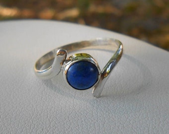 May include: A silver ring with a blue gemstone. The ring has a unique, curved design.