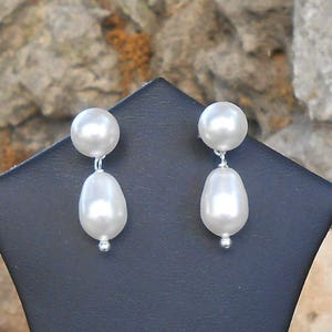 May include: A pair of white pearl drop earrings. The earrings feature a small round pearl at the top and a larger teardrop-shaped pearl hanging below.