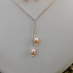 May include: A silver chain necklace with a delicate drop featuring two blush-colored pearls.